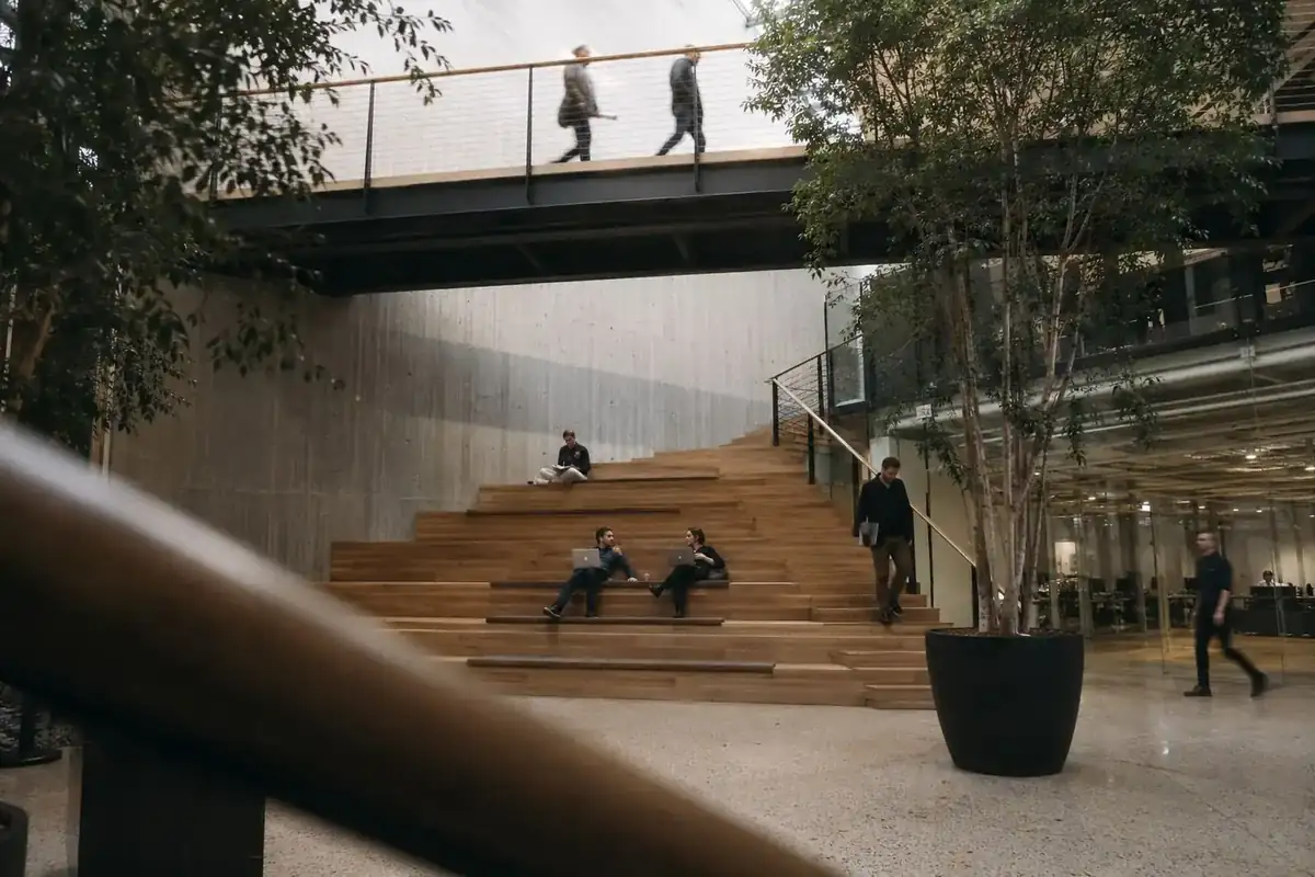 A bridge over an atrium above a wide timber stair where people sit working